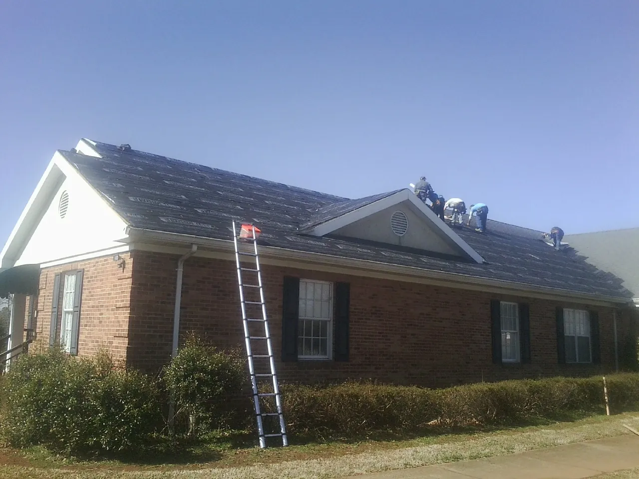 Crew tearing shingles off a brick ranch roof with a ladder set — Metal Roof Repair work by our crew in Lake Hughes