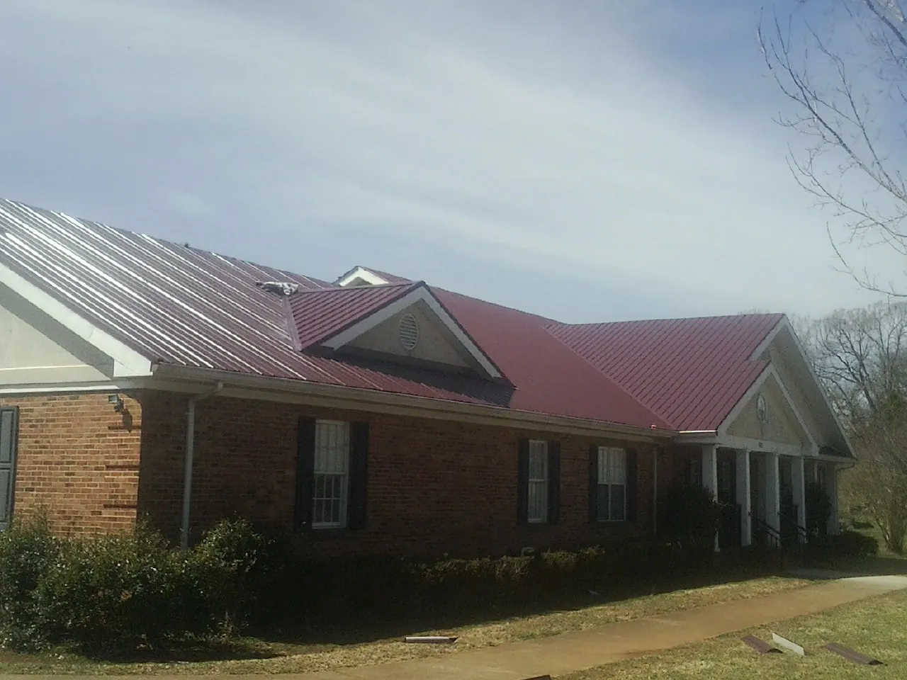 Red metal roof with gabled entries on a long brick building, from a Hail Damage Roof Repair job in Lake Hughes