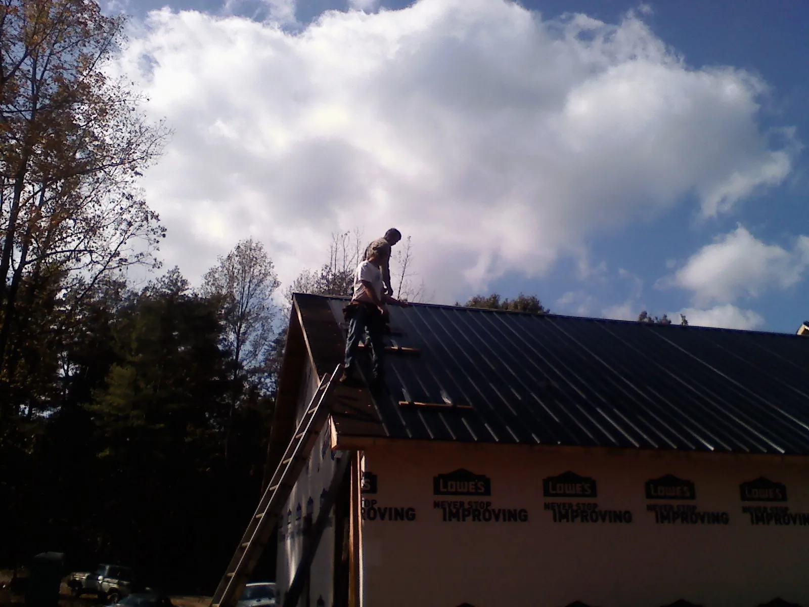 Roofer fastening dark metal panels high against a cloudy sky, from a Roof Inspection job in Lake Hughes