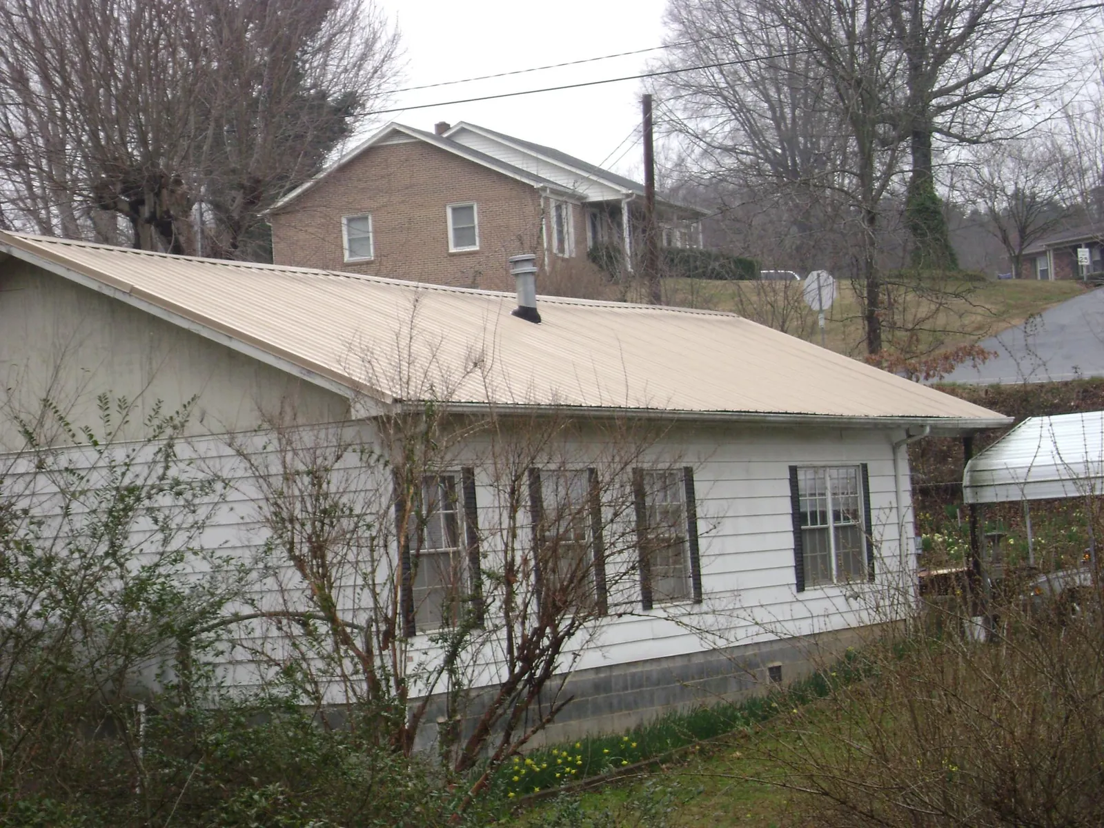 Tan metal roof on a white sided house set into a hillside — Commercial Roofing by Roofing Brothers in Lake Hughes